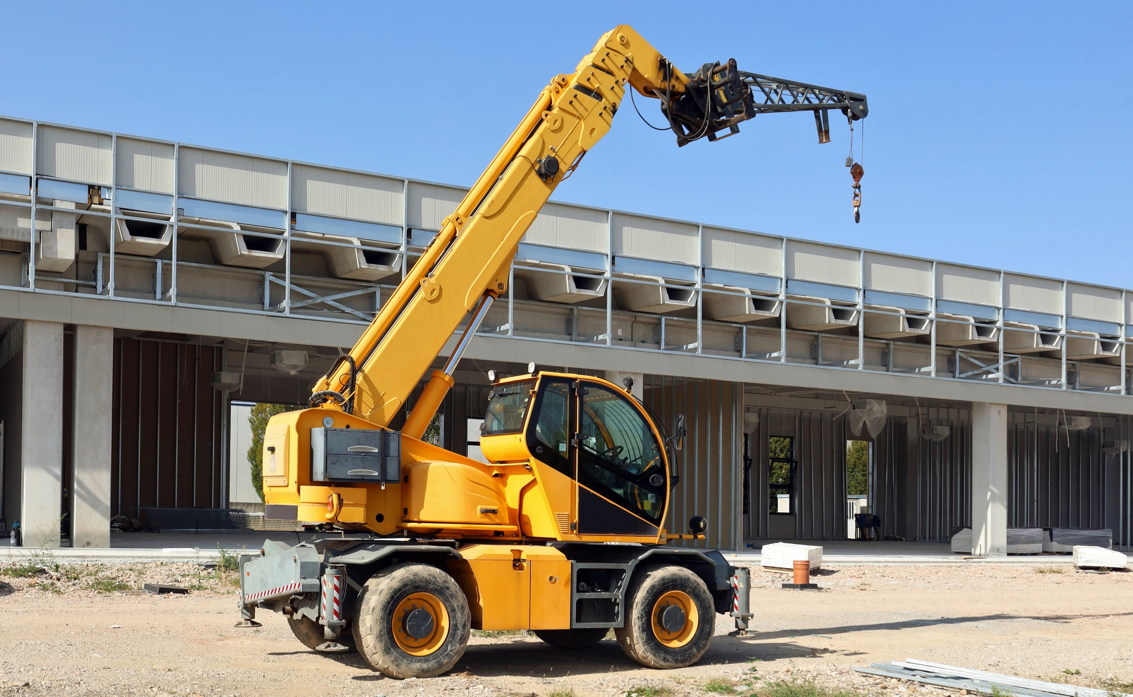 Yellow rotating telehandler at work in front of new commercial building under construction.