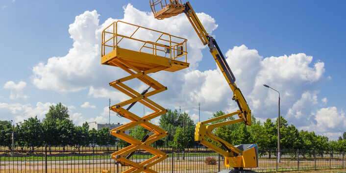 Yellow self propelled articulated boom lift and scissor lift on background of street with trees and sky