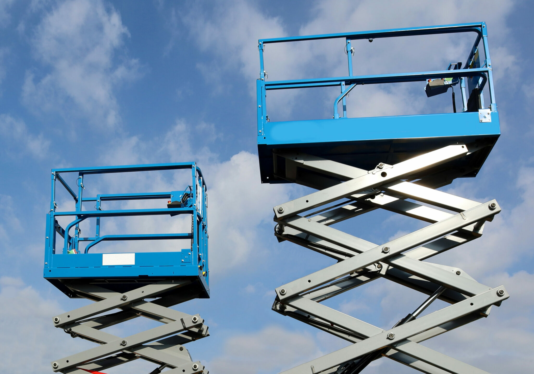 Two working platforms, called  scissor elevator, against blue sky with clouds.